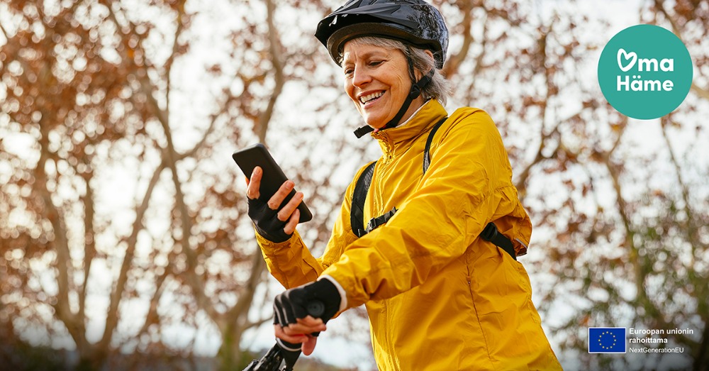 Nainen on pyöräilemässä ja katsoo hymyillen puhelintaan.